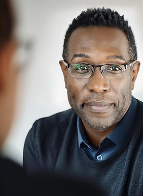 Black smiling man, Michael Johnson, wearing glasses and a dark jumper, sitting with two people during a couple’s session