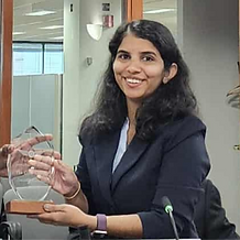 Young woman in a black suit blazer receiving an award wit ha smile on her face. Smrithy the Gate Keeper
