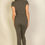 Thumbnail: A person wearing a fitted, short-sleeve, olive green jumpsuit is standing with their back facing the camera against a plain,