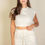 Thumbnail: A woman with long brown hair wears a sleeveless white crop top and matching high-waisted pants.