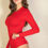 Thumbnail: Woman with long brown hair wearing a fitted, long-sleeve red bodysuit, posing against a plain light background.