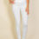 Thumbnail: A woman stands against a beige background, wearing a white fitted top, white skinny pants, and white shoes, with one hand res