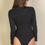 Thumbnail: A woman with long brown hair wears a black, long-sleeve bodysuit and faces away from the camera against a neutral background.