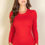 Thumbnail: Woman with long brown hair wearing a fitted, long-sleeved red top, standing against a neutral background.