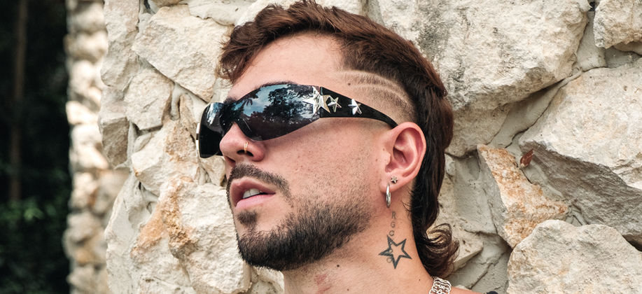 Duque wearing glasses and a black tank with a  rock textured background