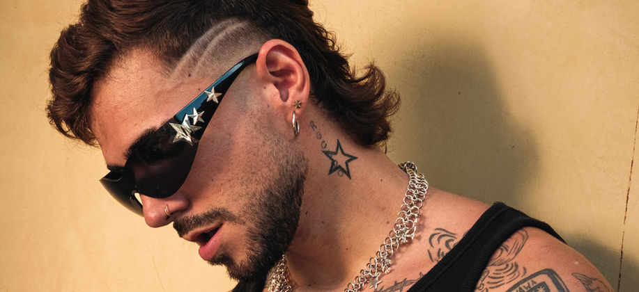 Duque wearing glasses and a black tank with a mustard plain background