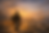 A painterly image of a lone traveler walking along a rugged path through a mountainous landscape at sunset. The figure wears ancient robes and carries a staff and sack, silhouetted against a golden sky. In the distance, cities rise on hills, tents and animals mark a resting place, and birds soar above. The scene evokes pilgrimage, solitude, and the mythic journey of faith across time.