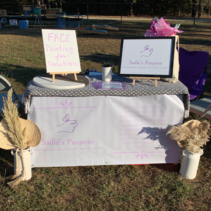 A table with signs for Sadie's Purpose and some decorative plants in front.