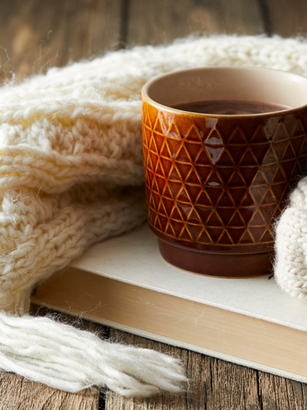 An orange mug sitting on a book surrounded by a knit white blanket