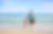 Man in blue shirt and girl in pink outfit holding hands, walking on sandy beach towards blue ocean under clear sky. Relaxing scene.