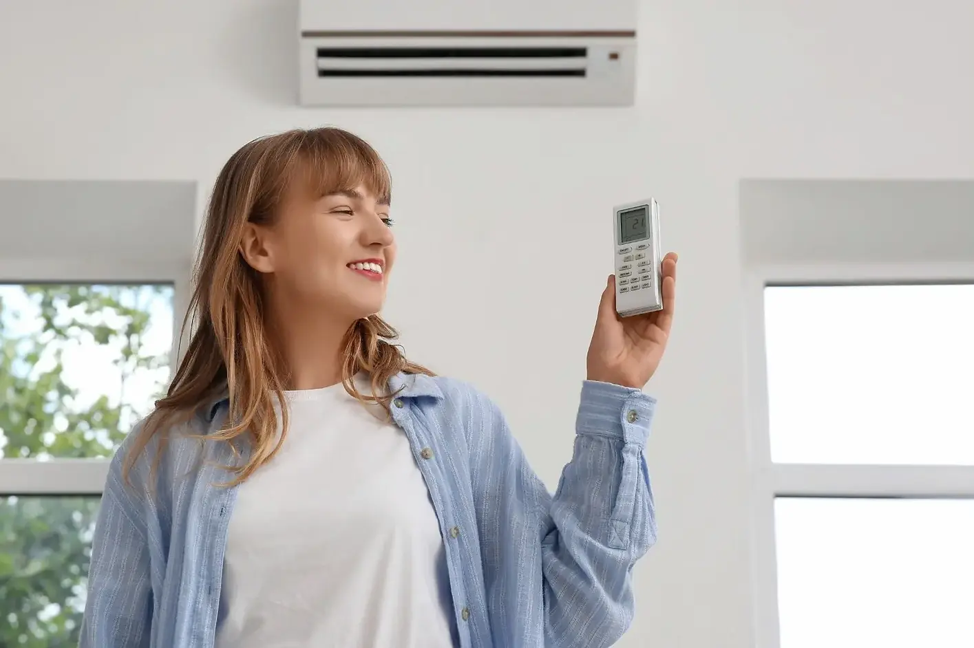 Woman using a remote to set a ductless mini-split heat pump to 21°C in a bright living room