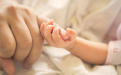 Hand eines Neugeborenen umgreift den Finger eines Erwachsenen