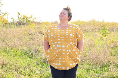 Smiling plus size woman standing in a naturalized field, with her hands in her oversized decorative tunicpockets