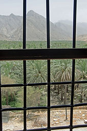 Oman, Blick durchs Fenster in einen Palmengarten und Gebirge.jpg