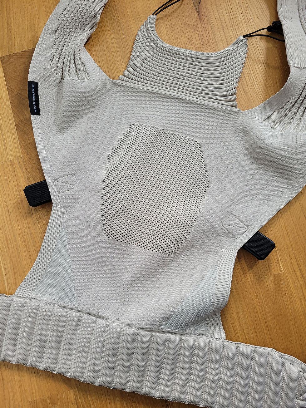 Graue Strick-Babytrage auf Holzboden, schwarzes Label mit www.flybabyberlin, gepolstert und leer. Testbericht Flybaby Babytrage