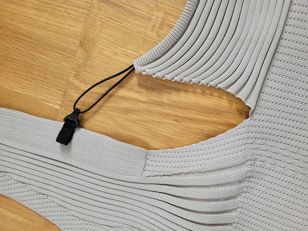 Nahaufnahme eines hellgrauen Strickteils mit schwarzer Kordel auf Holzfußboden. Testbericht Flybaby Babytrage