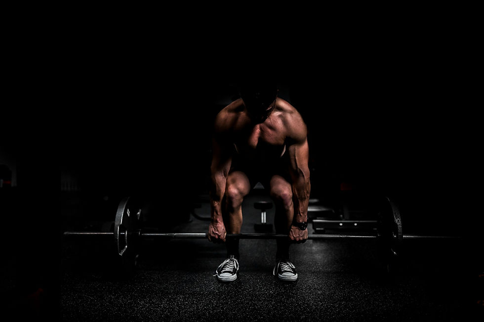 Muscular male athlete lifting a barbell from the floor in a dark gym