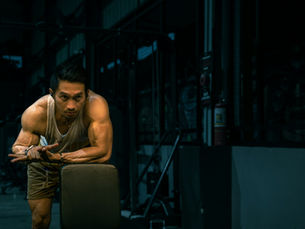 Fit male athlete resting against a barbell rack in a dark industrial gym, representing velocity-based strength training