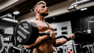 Muscular male athlete performing a barbell bicep curl in a dark industrial gym