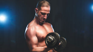 Lean muscular man performing a dumbbell curl in a dark studio