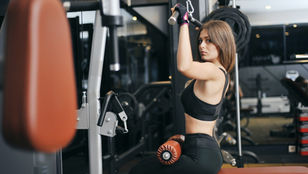 Fit female athlete performing a lat pulldown exercise in a modern gym, representing unilateral resistance training and cross-education strength transfer