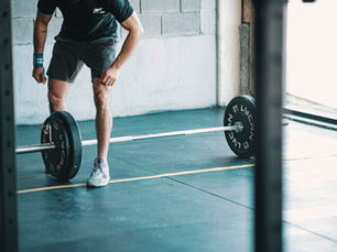 Lean, athletic man preparing to lift a loaded barbell in a bright industrial gym