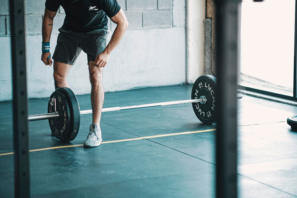 Lean, athletic man preparing to lift a loaded barbell in a bright industrial gym