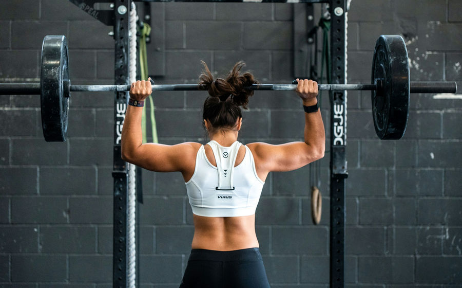 Fit woman pressing a barbell overhead in a gym