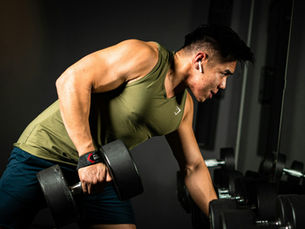 Athletic man performing a single-arm dumbbell row in a dark gym