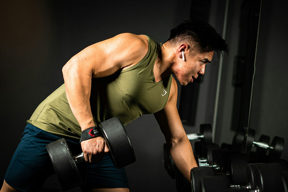 Athletic man performing a single-arm dumbbell row in a dark gym