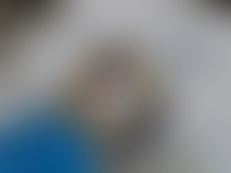Mão com luva azul segura protetor de máquina a laser sobre mesa, com ferramentas e pano ao fundo.