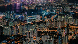 香港入境处——夜晚的香港城市景观充满活力，摩天大楼灯火辉煌，道路繁忙。海港倒映着城市灯光，构成一幅熙熙攘攘的都市景象。