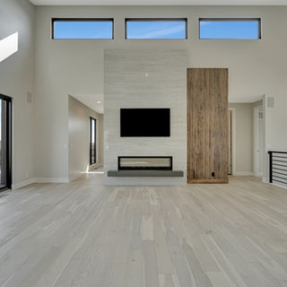 Spacious living room with light wood floor, modern linear fireplace, mounted TV, tall windows, and sliding glass door to deck.