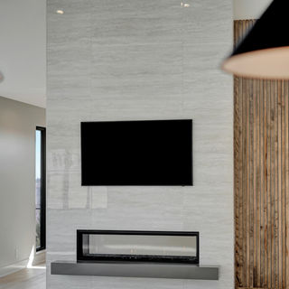 Tall fireplace with light gray stone surround, linear gas fireplace, mounted TV, wood accent wall, and light hardwood flooring.