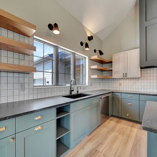 Murray Custom Homes designed kitchen with blue lower cabinets, open wood shelves, black sink, and geometric tile backsplash.