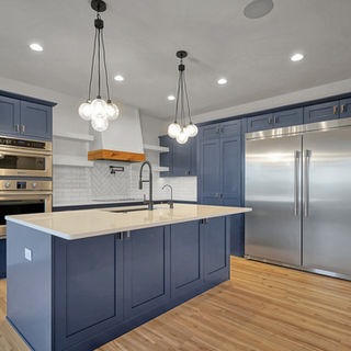 Modern kitchen with blue cabinets, stainless steel appliances, island sink, and pendant globe lights over wood flooring.