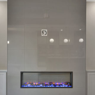 Sleek modern fireplace with gray glossy tiles, blue and orange flames, light carpet, and partial view of wall sconces and ceiling fan.