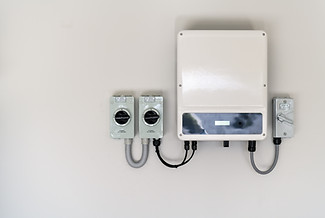 A solar inverter and DC isolator switches mounted on a wall, with labeled components for PV array and inverter isolation.