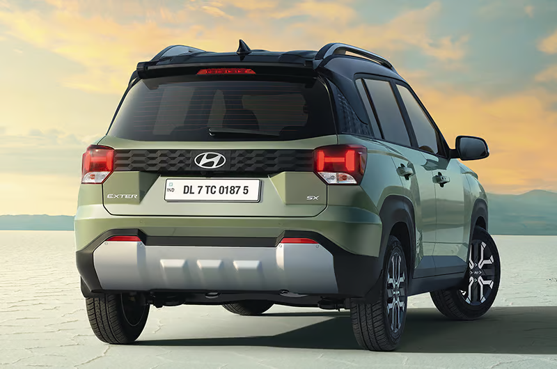 A green Hyundai SUV with a license plate at a desert-like setting under a sunset sky. Text on vehicle reads "Exter" and "SX."