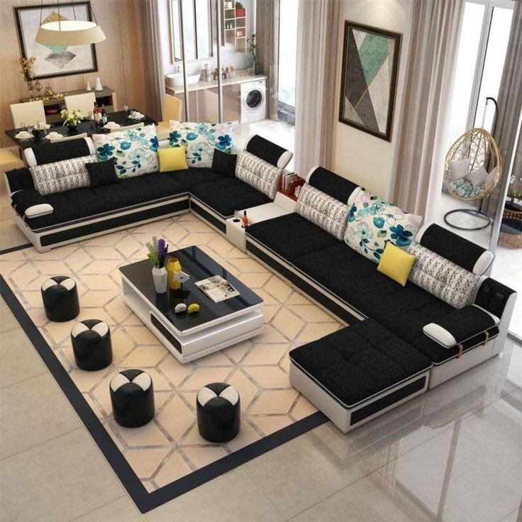 Spacious living room with a black U-shaped sofa featuring floral pillows, a geometric rug, a modern coffee table, and dining area in the back.