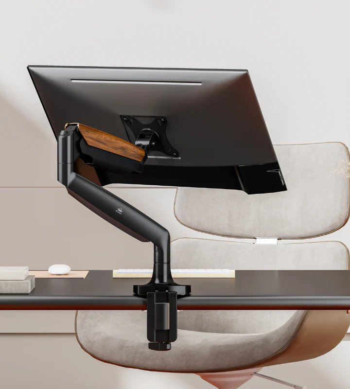 A sleek black monitor arm holds a tilted screen on a modern desk. Gray chair, white keyboard, books, and a mouse are visible. Minimalist setup.