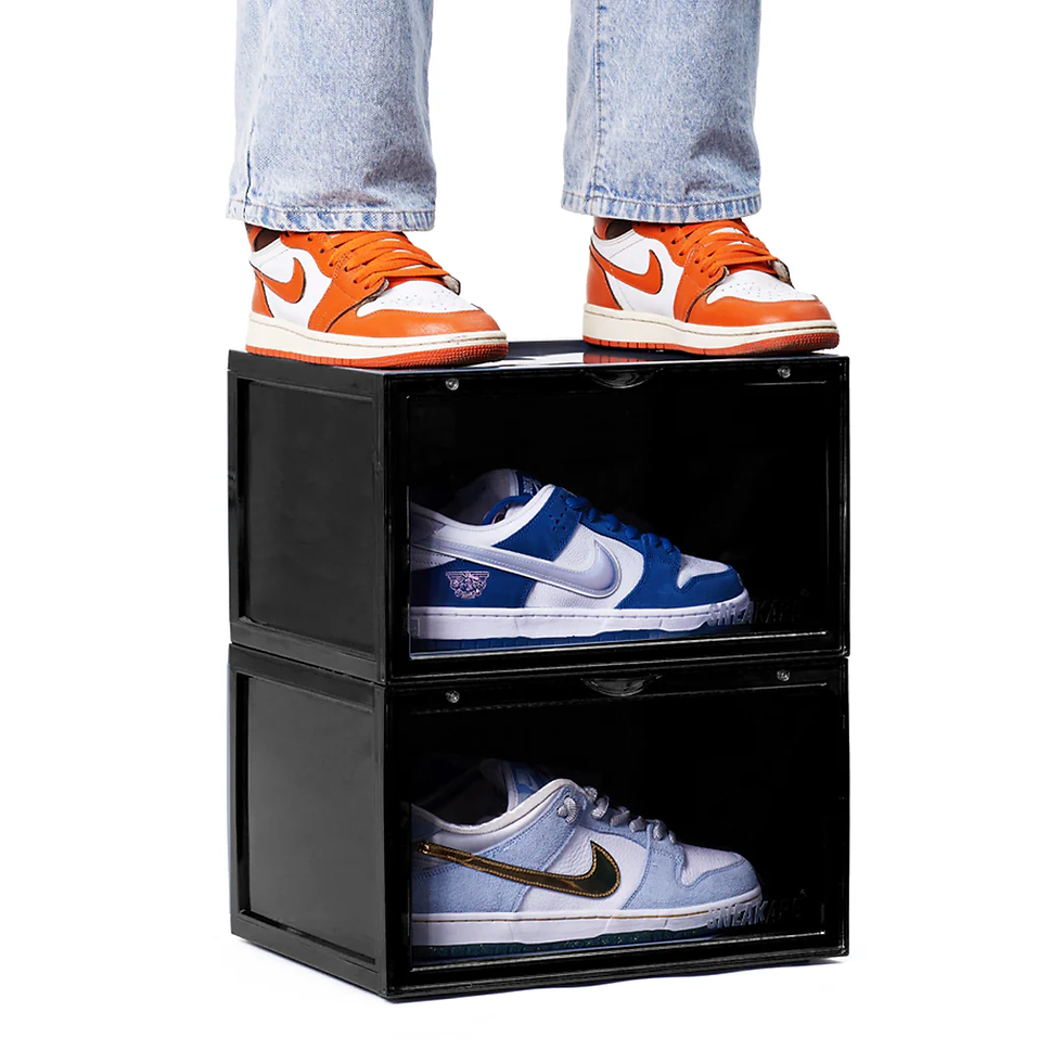 Person in jeans wearing orange sneakers stands on black shoe boxes with visible blue and white sneakers inside, against white background.