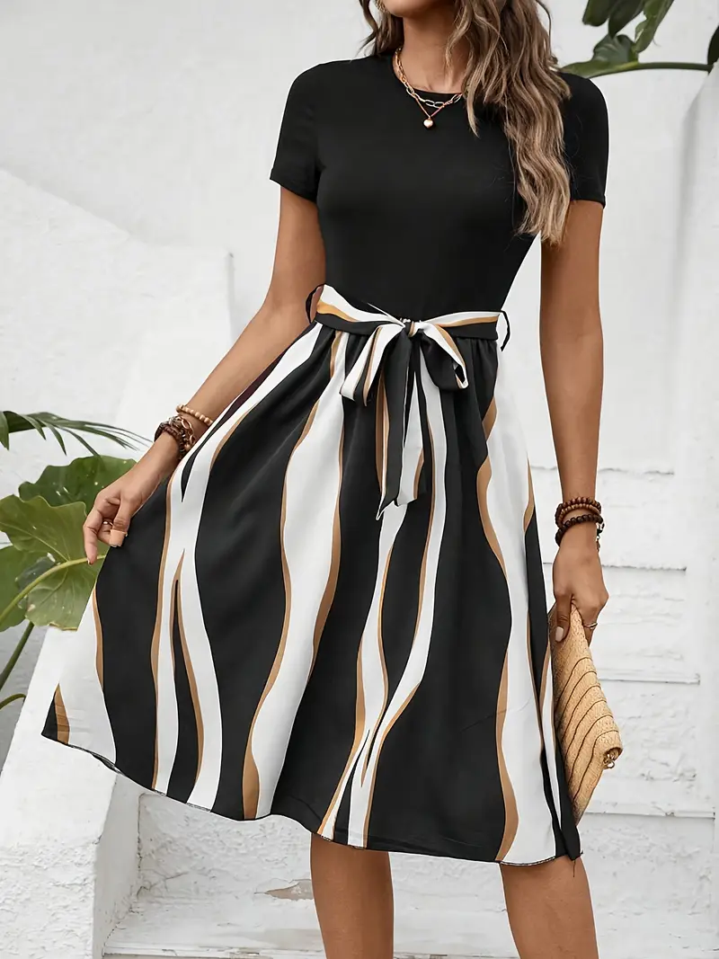 Woman in a black top with a striped skirt, holding a woven clutch in a bright setting. Skirt features black, white, and brown wavy lines.