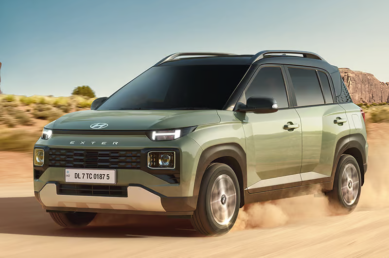 Green SUV driving on a dusty road in a desert landscape. The car is labeled "EXTER" with a visible license plate. Clear sky above.