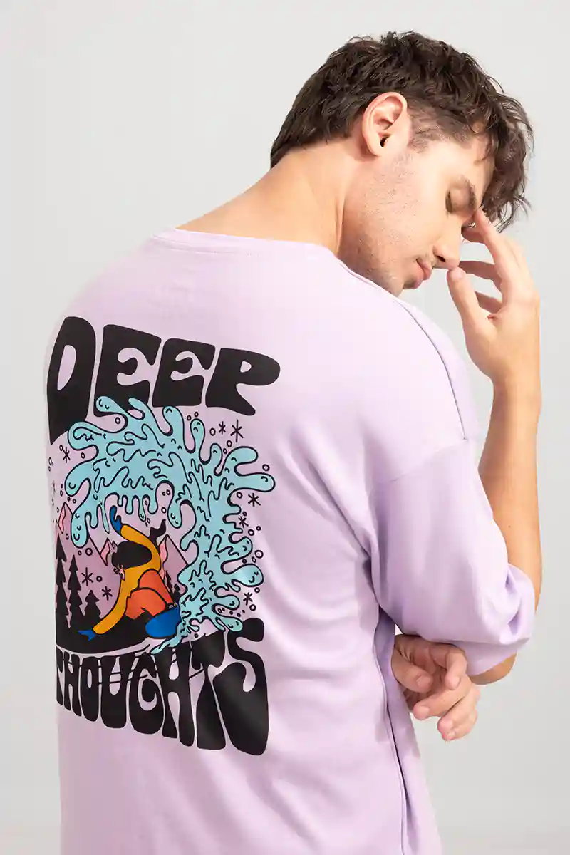 Man in a lavender shirt with colorful surf design and text "DEEP THOUGHTS," touching his face. Neutral background. Relaxed mood.