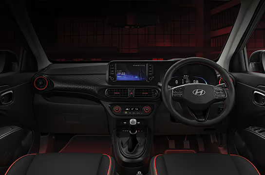 Car interior view with a black dashboard, touchscreen display showing "11:22," and Hyundai logo on the steering wheel. Red accent lighting.