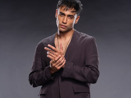 Studio portrait of Armaan Khera in a dark suit, clasping his hands against a gray background.