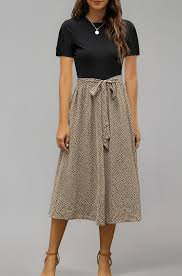 Woman wearing black top, beige polka dot skirt with bow, standing against a gray background. No visible text. Simple, elegant mood.