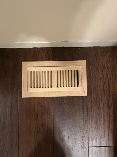 Close-up of a custom oak hardwood vent cap cut flush into dark-stained hardwood flooring, showing seamless craftsmanship and attention to detail.