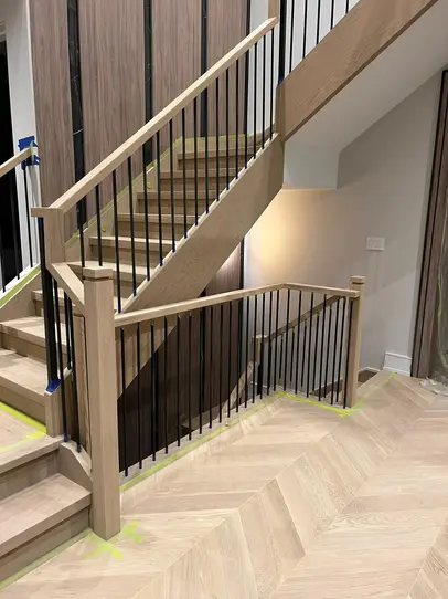 Chevron oak flooring paired with an open-riser staircase featuring black iron spindles and light oak treads in a modern entryway.